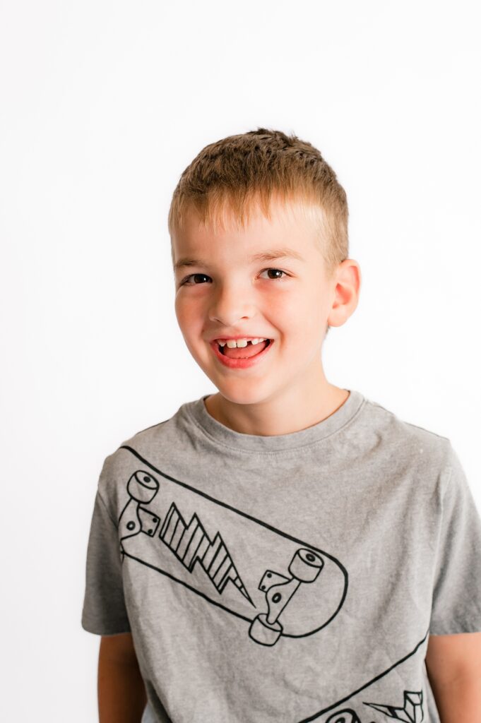 Houst school portrait photography depicts a young boy in a gray t-shirt smiling before a white background
