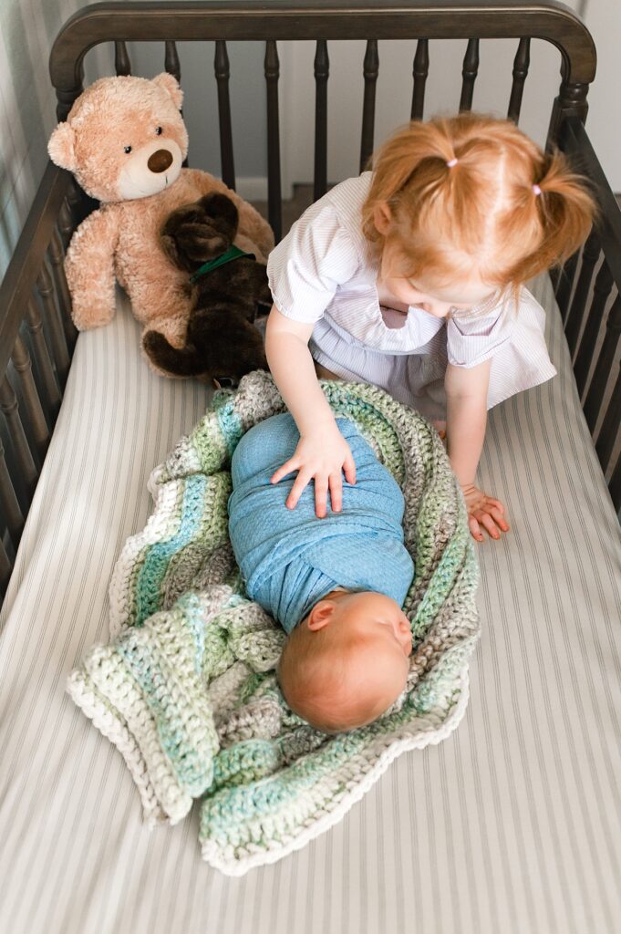 A toddler admires her baby brother in his crib during Houston In Home Lifestyle Newborn Photography session