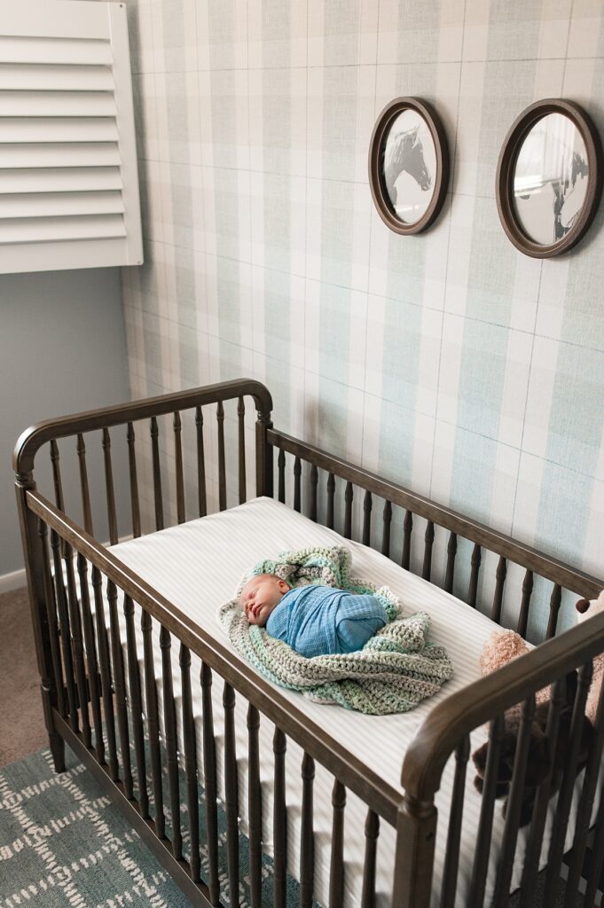 A baby sleeps in a Houston Vintage Western Nursery featuring green plaid wallpaper and vintage horse photos