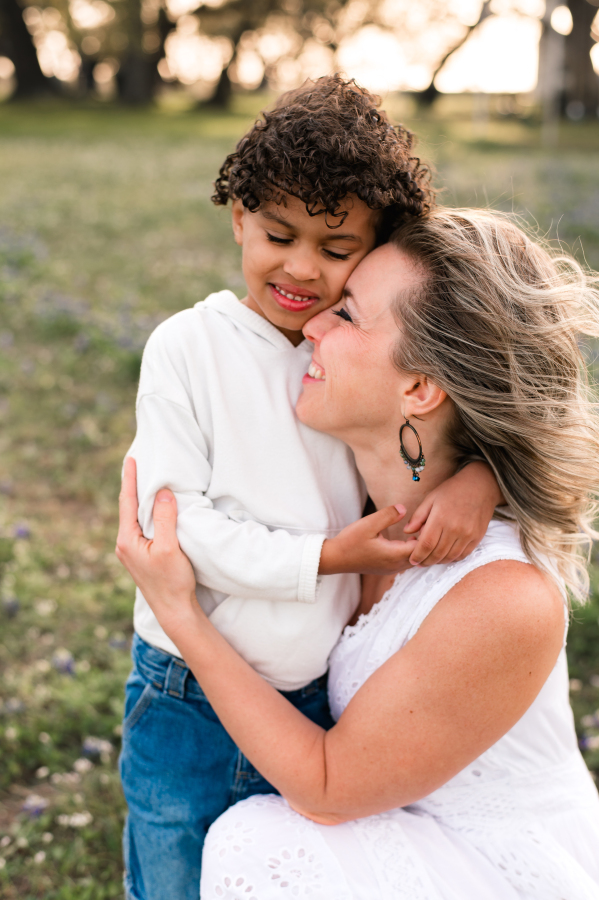 A mother snuggles her son during family photos surrounded by bluebonnets in brenham tx