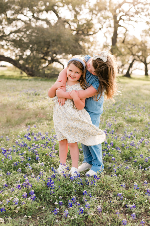 Sisters embrace at golden hour in surrounded by Brenham TX bluebonnets