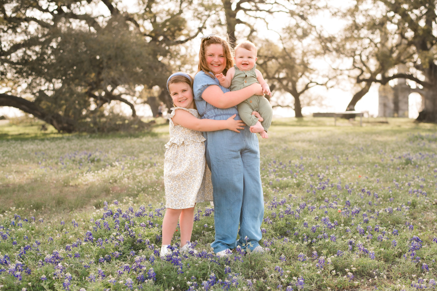 Three children are photographed at golden hour surrounded by bluebonnets in brenham tx
