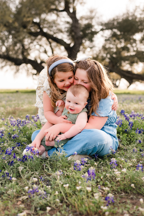 Sisters hold their baby sibling in a field of bluebonnets in brenham tx