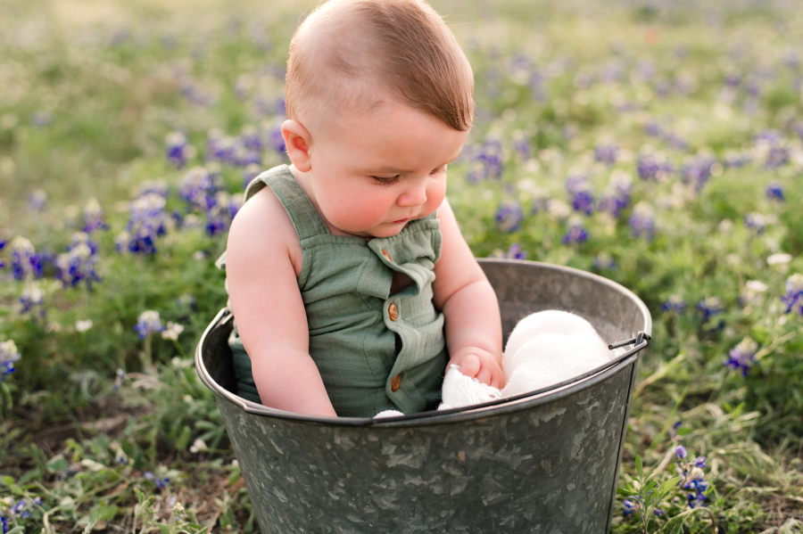 A baby wearing a green romper is seated in a tin pail for bluebonnet photos texas