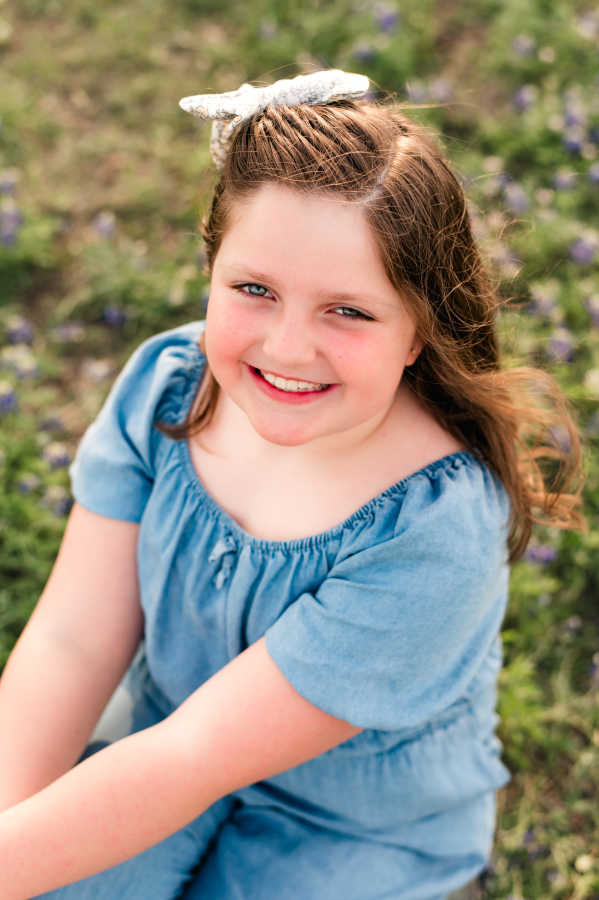 A young girl wearing a denim outfit is seated on the ground with bluebonnets in brenham tx