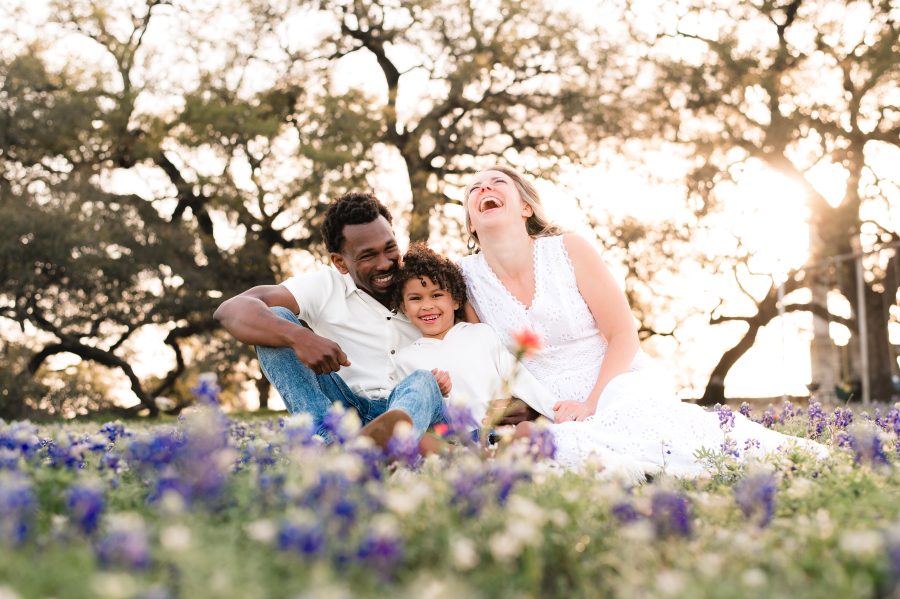 A family of three laugh in a field of bluebonnets in brenham tx