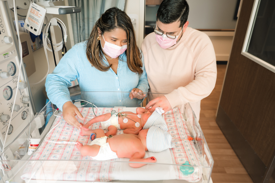 New parents smile down at their newborn twin girls during a first 48 newborn photography shoot at Houston Methodist
