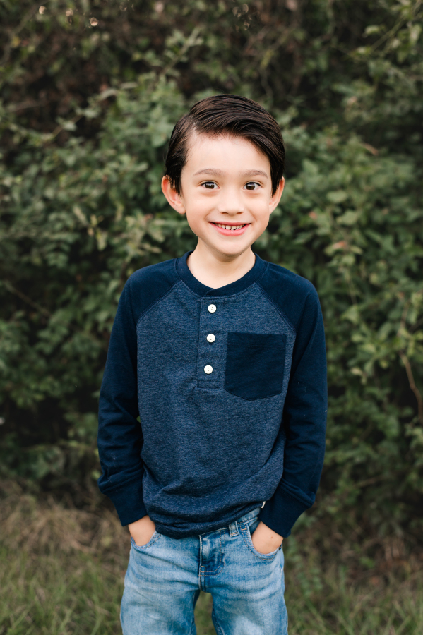 A portrait taken in Bridgeland Cypress Texas showcases a young boy smiling with his hands in the pockets of his jeans 