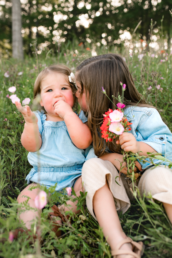 Young sisters wearing denim pose in a field of flowers in a city park houston texas. 