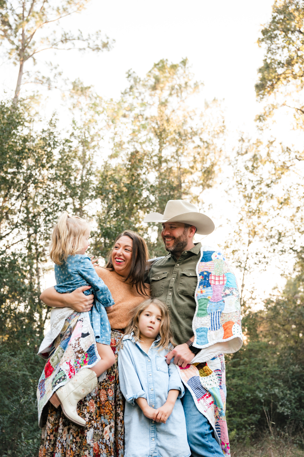 A kid friendly Houston guide shows a family of four smiling while wrapped in a quilt during a session with a local Cypress family photographer. 