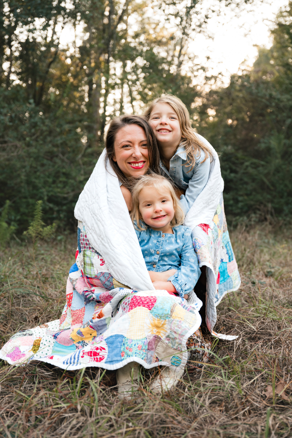 A mother holds her daughters wrapped in a family quilt in a photo shown in a guide for kid friendly houston tx activities. 