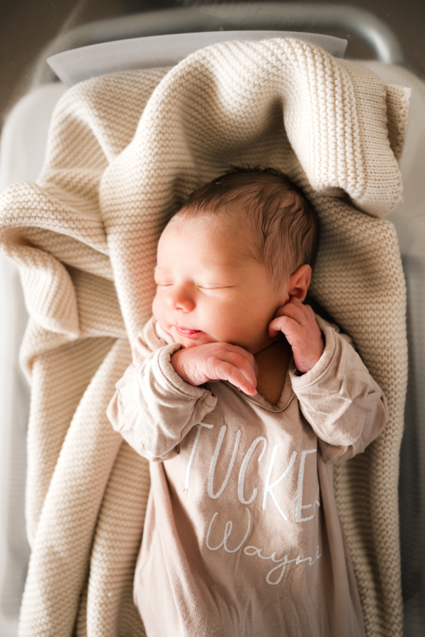 A newborn baby sleeps on a knitted baby blanket during a Houston Fresh 48 photoshoot