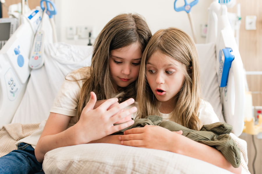 Older sisters snuggle their newborn baby brother from a Houston hospital bed during a Fresh 48 session with Houston newborn photographer