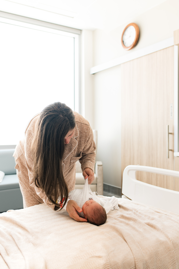 A mother swaddles her newborn baby in their hospital room during a Fresh 48 newborn session in Houston TX