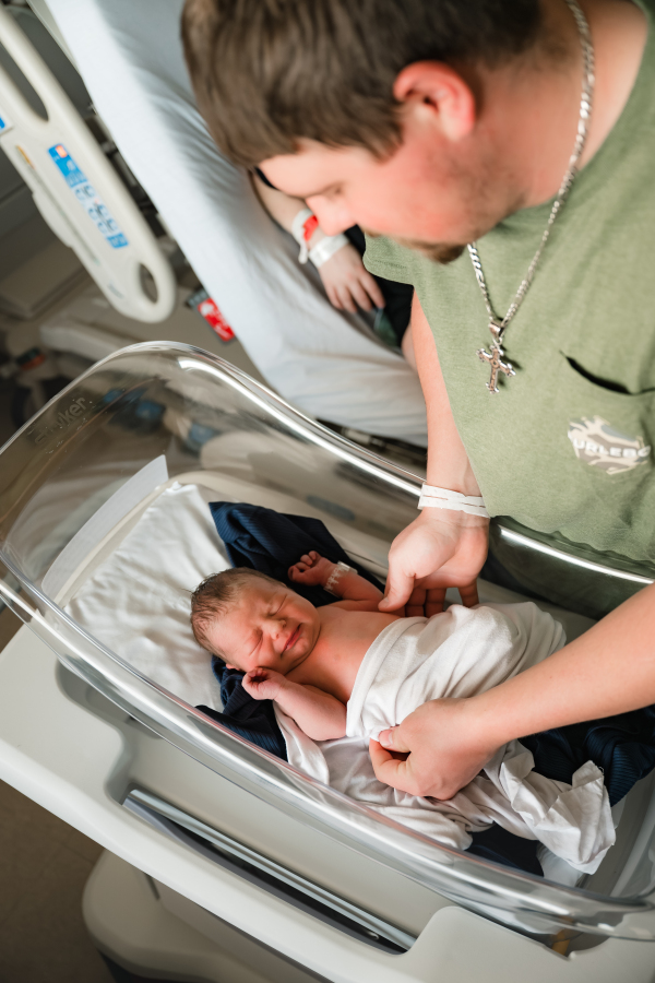 A new father dresses his newborn in the baby's hospital bassinet during a Houston newborn fresh 48 session