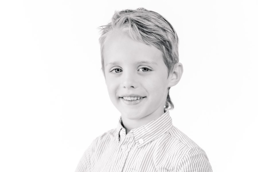 A black and white Houston school portrait shows a young boy wearing a striped button up standing before a white background.