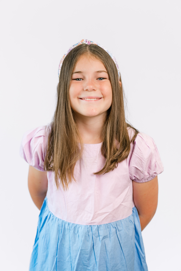 An elementary aged girl smiles in a pink and blue dress for Houston school pictures.