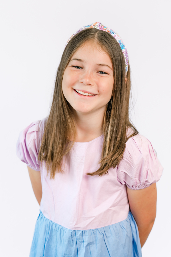 A young girl smiles in front of a white background for a modern school portrait taken by a Houston school photographer.