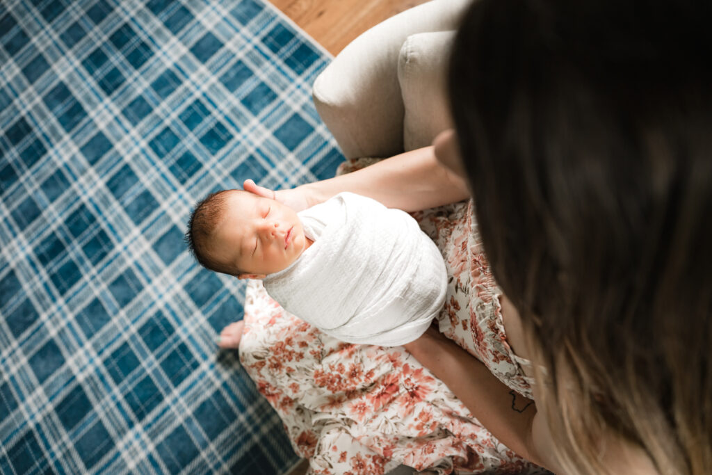 A swaddled newborn baby is held in his mother's lap, demonstrating newborn poses for photography sessions in Houston.