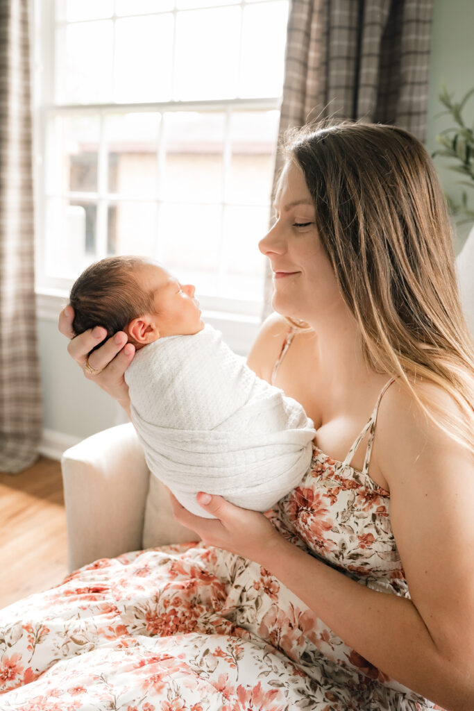 A mother smiles at her swaddled newborn baby during newborn nursery photos in Houston. 