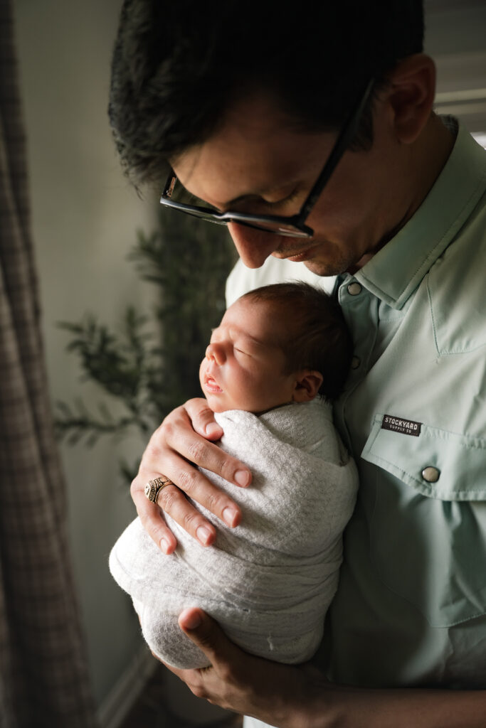 A Houston TX father holds his swaddled son during newborn photos with dad. 
