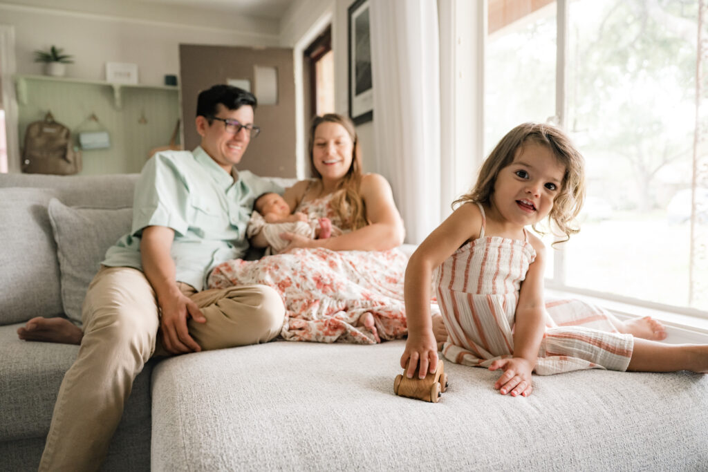 A family of four is photographed on their sofa, demonstrating newborn poses for photography sessions in the home in Houston. 