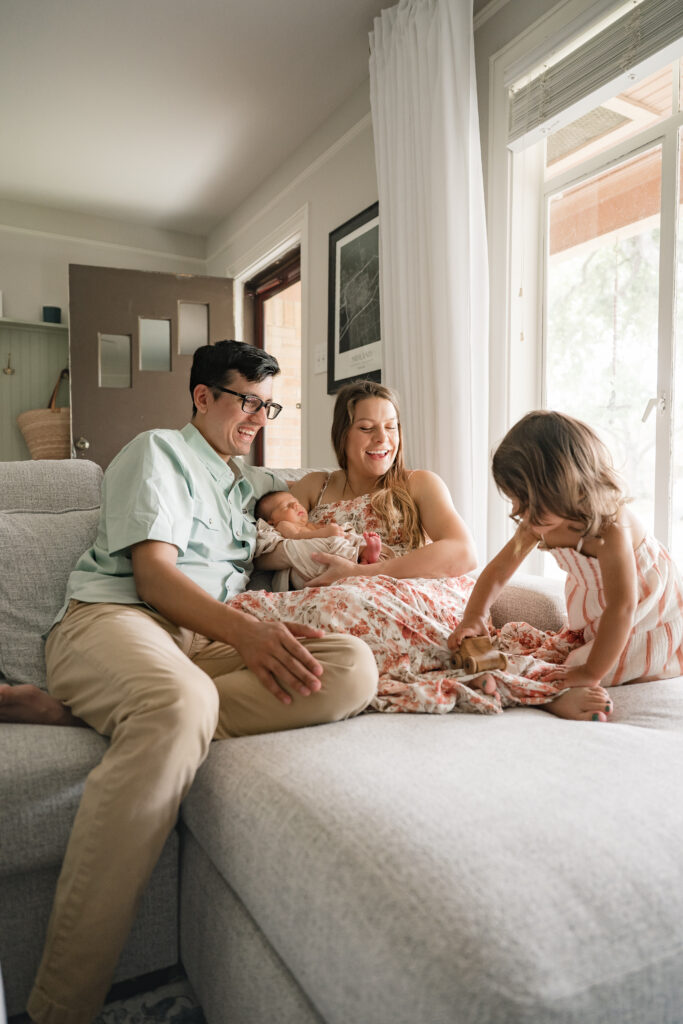 A family relaxes on their couch with their older daughter and newborn son during an in-home houston newborn photography session.