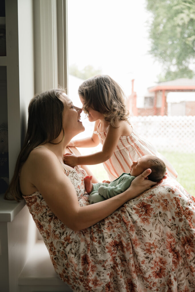 A mother & her daughter smile as mom holds her newborn son during an in-home houston newborn photography session.