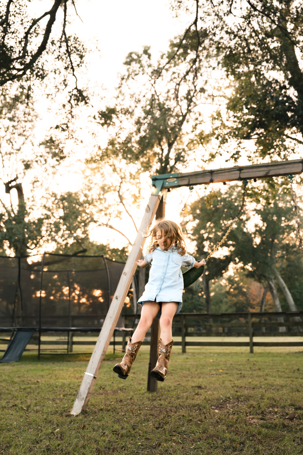 A young girl in a blue dress jumps out of a backyard swing during a lifestyle Houston famly session.