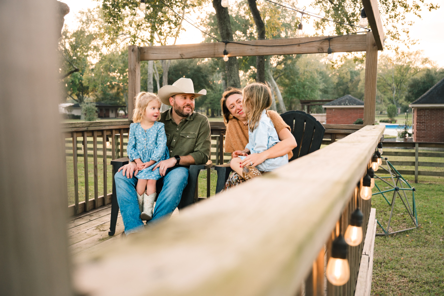Two young girls sit on the laps of their parents on their back porch during a session with a Houston lifestyle photographer.