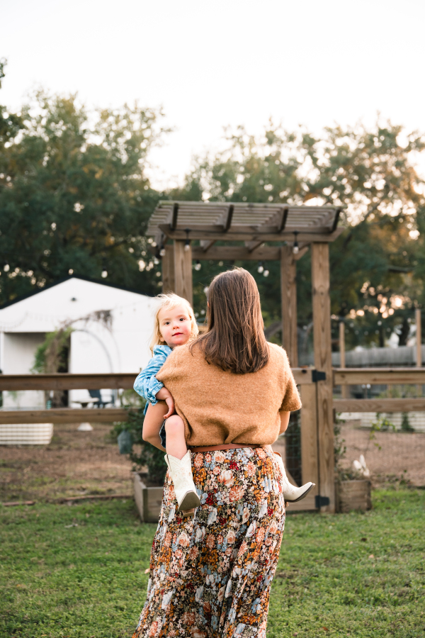 A mother carries her toddler in her arms toward the family chicken coop in a photoshoot with a Houston lifestyle photographer.