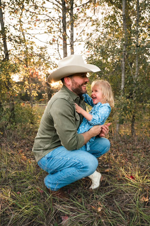 A toddler girl laughs as her father smiles in a photo taken by a Houston lifestyle photographer.