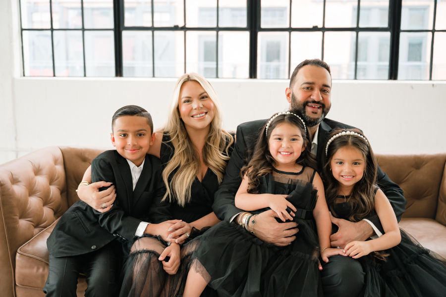 A family of 5 wearing black attire are seated on a leather sofa in a photography studio in Houston TX.