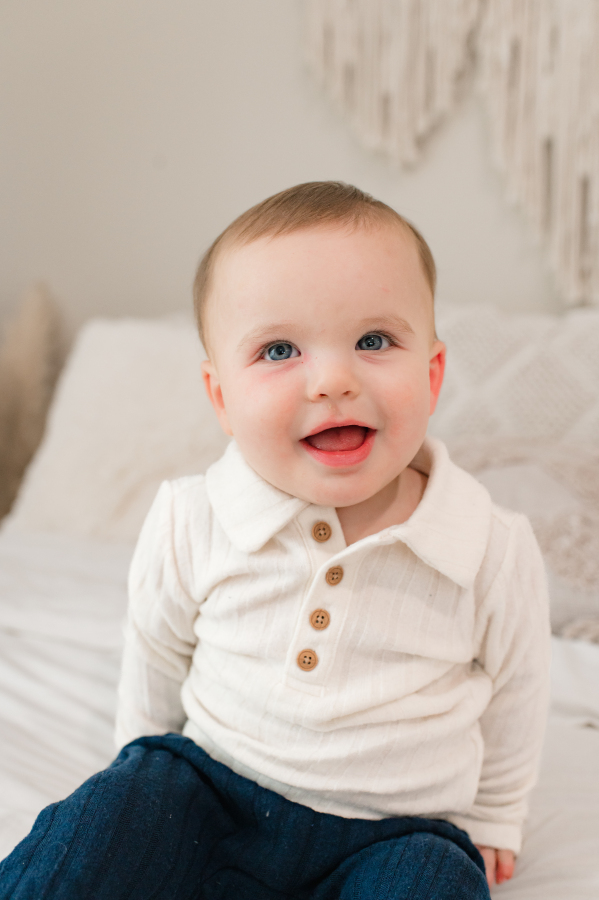 An infant is photographed smiling atop a cream blanket in a family photography studio in Houston Texas.