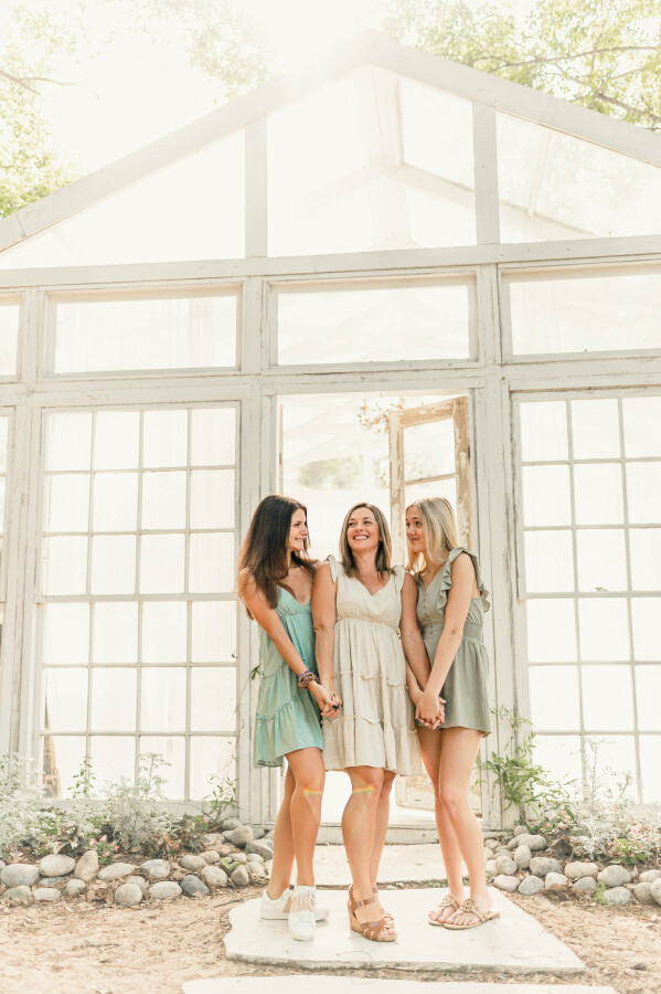 Three young women hold hands outside a glass house at The Oak Atelier, a photography studio in Houston TX.